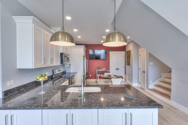 kitchen featuring dark stone countertops, white cabinetry, a sink, appliances with stainless steel finishes, and a peninsula