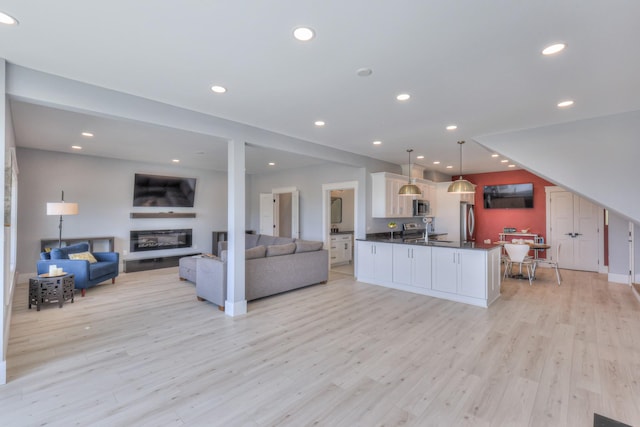 living area with a glass covered fireplace, recessed lighting, and light wood finished floors