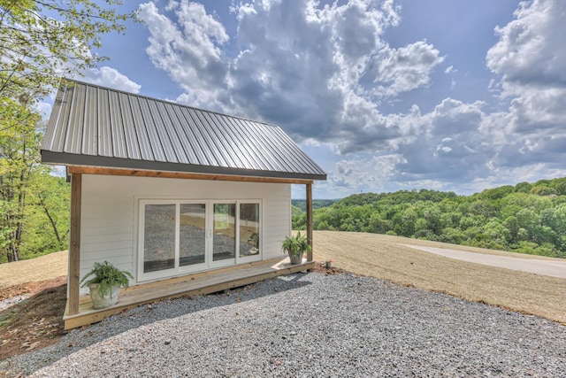 view of home's exterior with an outdoor structure, metal roof, and a view of trees