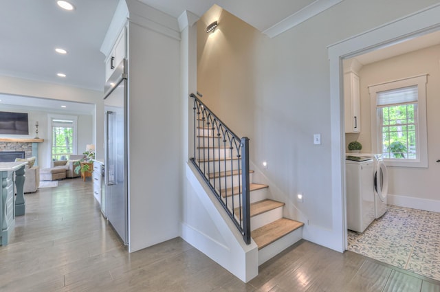stairs with recessed lighting, independent washer and dryer, a stone fireplace, baseboards, and wood finished floors