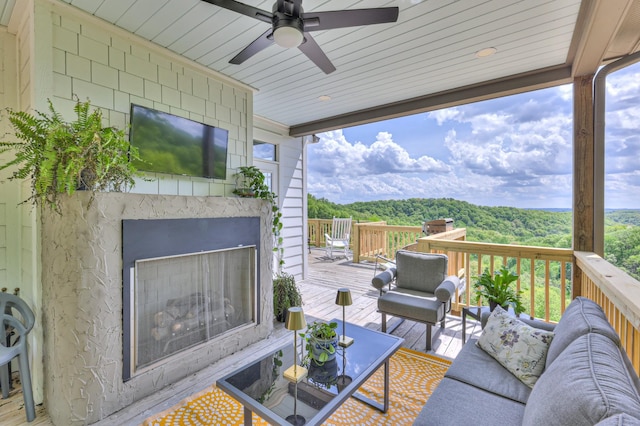 wooden deck with ceiling fan and an outdoor living space with a fireplace