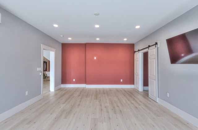 unfurnished room with baseboards, a barn door, light wood-style floors, and recessed lighting
