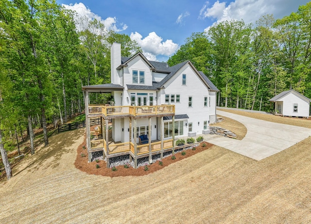 back of property featuring driveway, roof with shingles, a chimney, and a deck