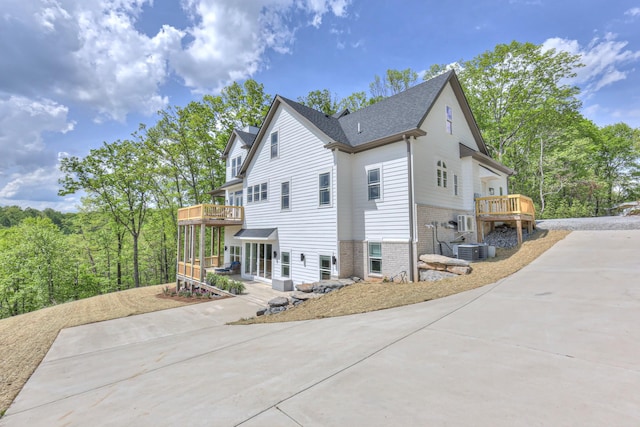 view of home's exterior with brick siding, driveway, a wooden deck, and central air condition unit