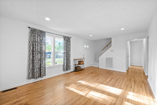 unfurnished living room with a textured ceiling, visible vents, light wood-type flooring, and stairway