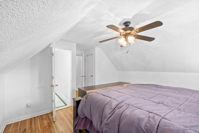 bedroom with baseboards, wood finished floors, a textured ceiling, and vaulted ceiling
