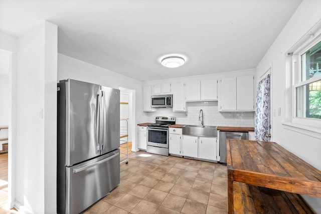 kitchen with butcher block counters, white cabinetry, stainless steel appliances, and a sink