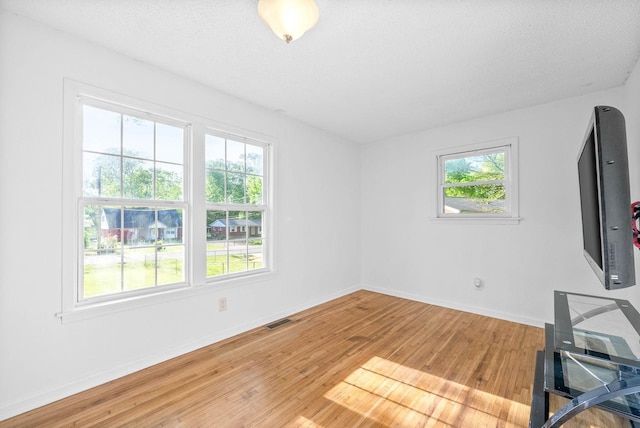 unfurnished living room featuring light wood finished floors, visible vents, a wealth of natural light, and baseboards