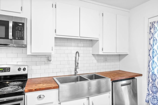 kitchen with wood counters, white cabinets, a sink, stainless steel appliances, and backsplash