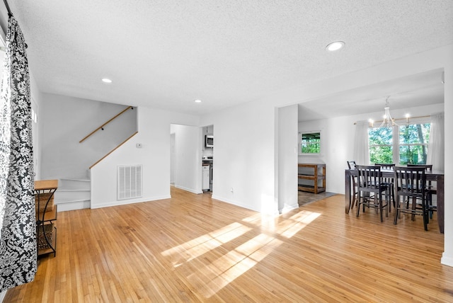living area with stairway, a chandelier, light wood-type flooring, visible vents, and a textured ceiling