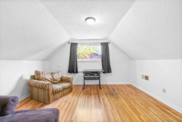 sitting room featuring light wood finished floors, visible vents, vaulted ceiling, baseboards, and a textured ceiling