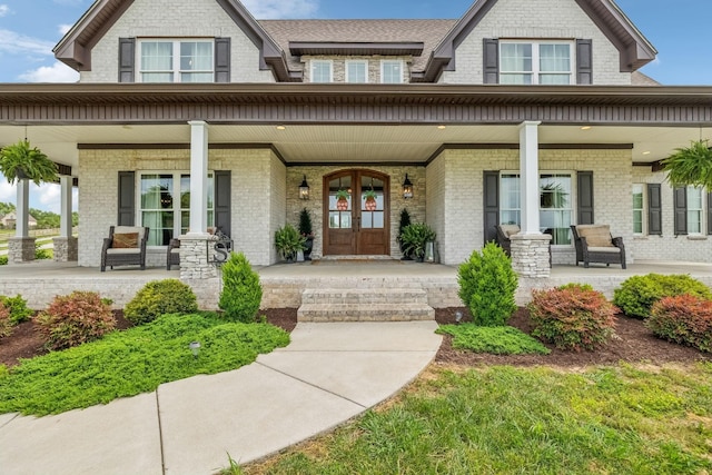 view of exterior entry with a porch, french doors, and brick siding