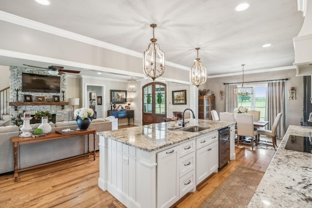 kitchen featuring a kitchen island with sink, a sink, light stone counters, light wood-style floors, and white cabinetry