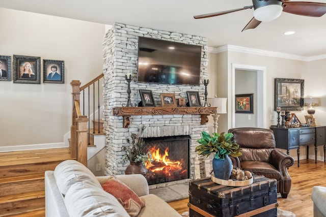 living area featuring crown molding, ceiling fan, a large fireplace, baseboards, and wood finished floors