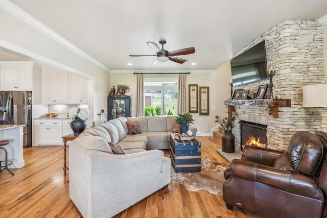 living room with a ceiling fan, a stone fireplace, ornamental molding, and light wood-style floors