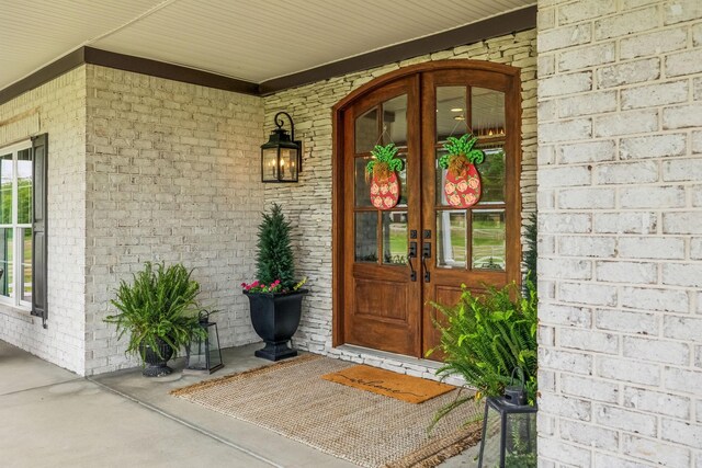 view of exterior entry featuring french doors, covered porch, and brick siding