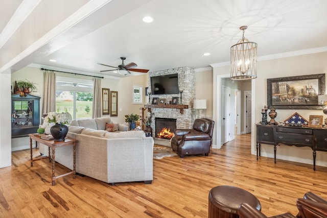 living area with crown molding, light wood finished floors, a stone fireplace, ceiling fan with notable chandelier, and recessed lighting