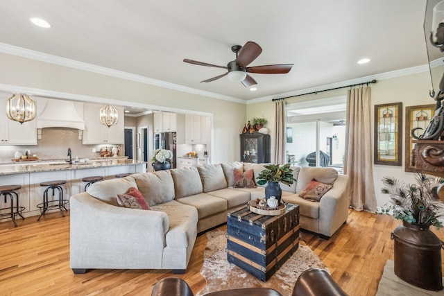 living room featuring crown molding, recessed lighting, ceiling fan with notable chandelier, and light wood-type flooring