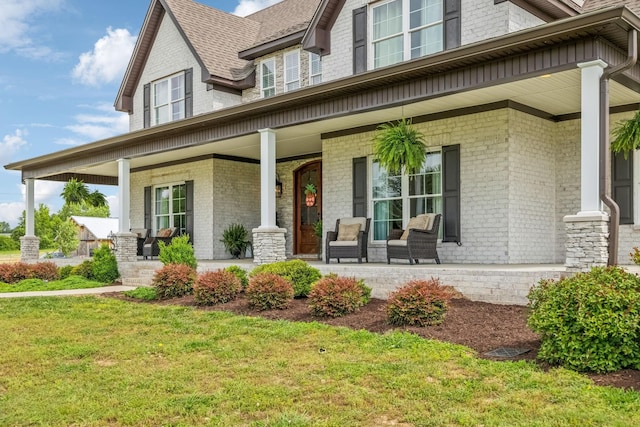 entrance to property featuring brick siding, roof with shingles, a yard, and covered porch