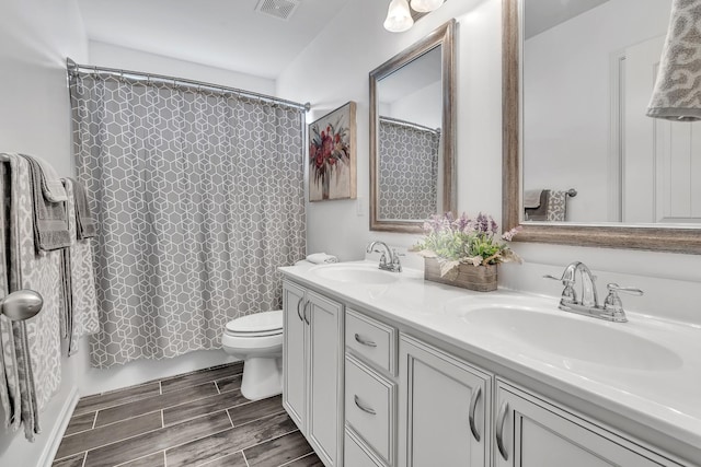 full bathroom with toilet, double vanity, a sink, and visible vents