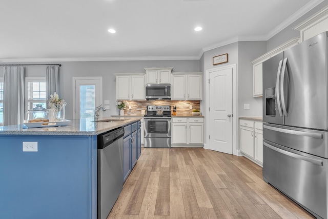 kitchen with a sink, stainless steel appliances, tasteful backsplash, light wood-style flooring, and white cabinetry