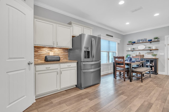 kitchen with light wood finished floors, visible vents, ornamental molding, and stainless steel fridge