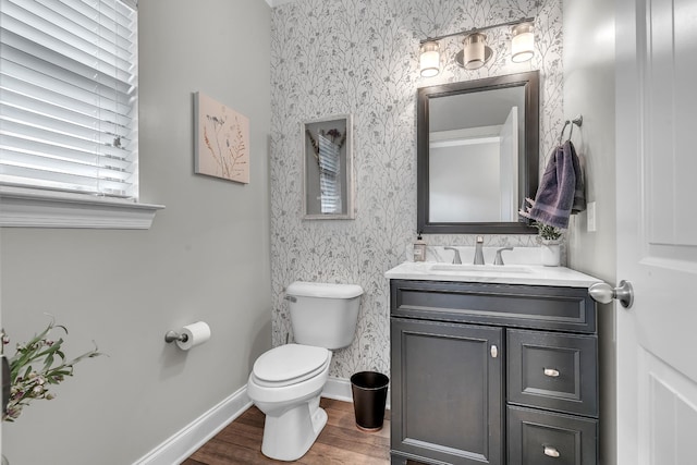 half bath with wood finished floors, vanity, toilet, and wallpapered walls