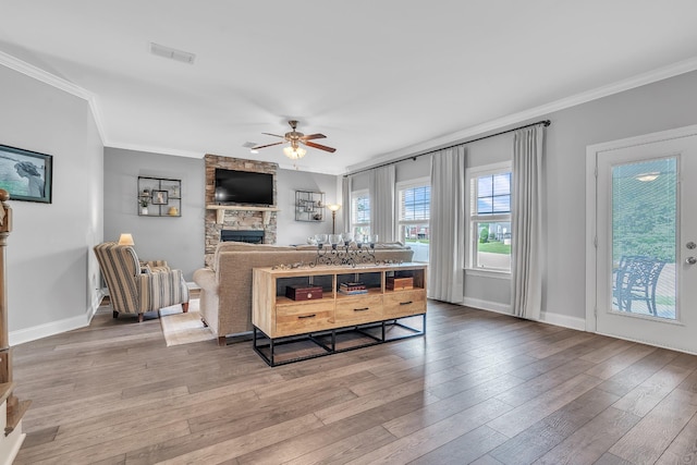 living room with a stone fireplace, wood-type flooring, visible vents, a ceiling fan, and crown molding