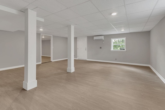 basement featuring light wood-style floors, baseboards, recessed lighting, an AC wall unit, and a paneled ceiling