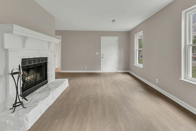 unfurnished living room with a high end fireplace, a wealth of natural light, wood finished floors, and baseboards