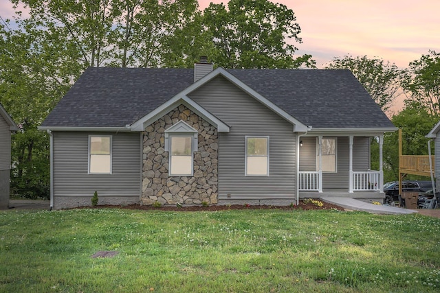 view of front of home featuring covered porch, a chimney, a front lawn, and roof with shingles