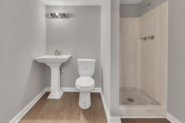bathroom with wood finished floors, toilet, a stall shower, and baseboards