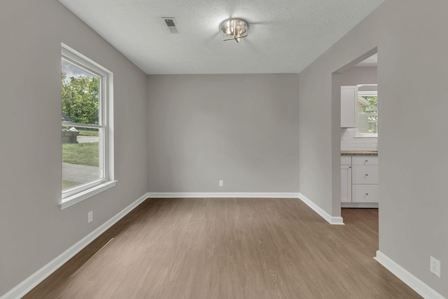 unfurnished room featuring wood finished floors, a healthy amount of sunlight, visible vents, and baseboards
