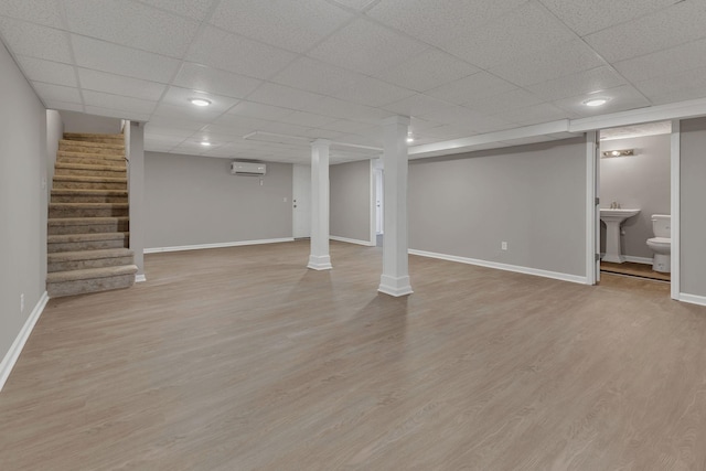 finished basement with a wall mounted air conditioner, stairway, a drop ceiling, and baseboards