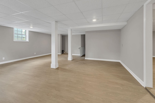 basement featuring wood finished floors, a drop ceiling, and baseboards