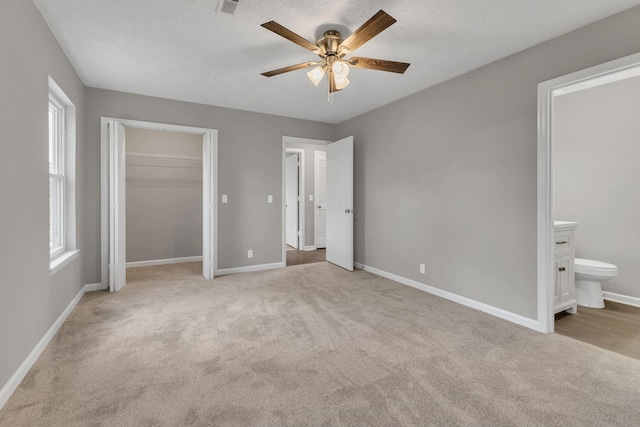 unfurnished bedroom featuring multiple windows, baseboards, ensuite bath, and light carpet