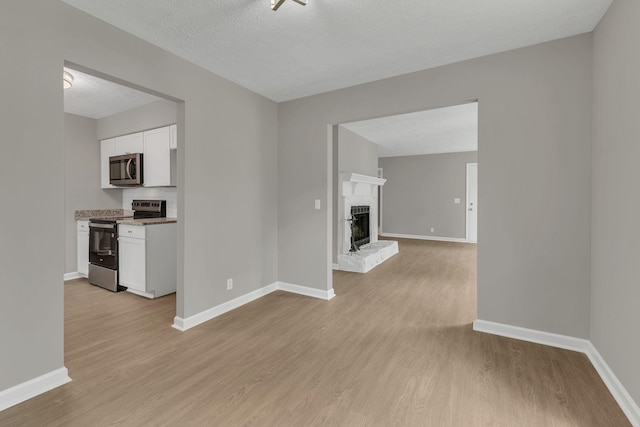 unfurnished living room with a fireplace, a textured ceiling, baseboards, and light wood-type flooring
