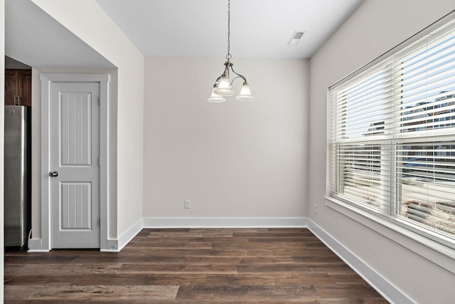 unfurnished dining area featuring dark wood finished floors, an inviting chandelier, baseboards, and visible vents