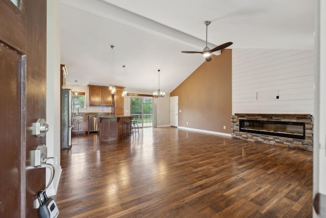 unfurnished living room with beamed ceiling, ceiling fan with notable chandelier, a fireplace, baseboards, and dark wood-type flooring