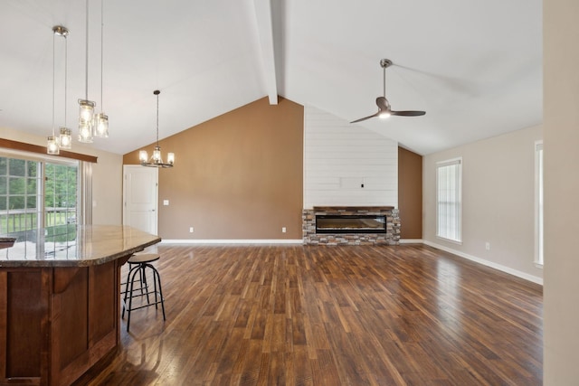 kitchen featuring vaulted ceiling with beams, ceiling fan with notable chandelier, a stone fireplace, dark wood-style flooring, and open floor plan