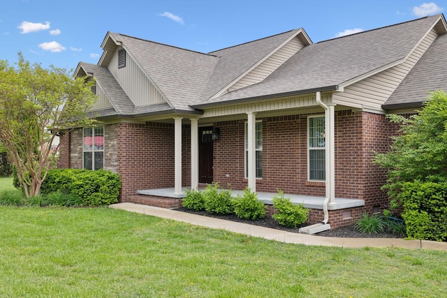 view of front facade with covered porch, brick siding, a shingled roof, and a front yard