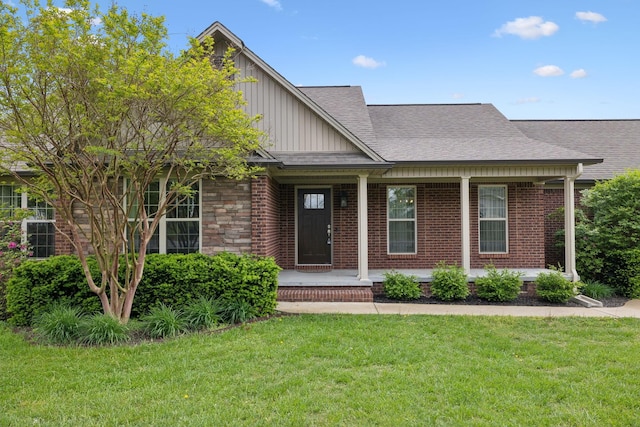 view of front of house with a porch, a front lawn, a shingled roof, board and batten siding, and brick siding