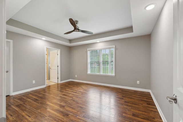 empty room with wood finished floors, ceiling fan, a tray ceiling, and baseboards