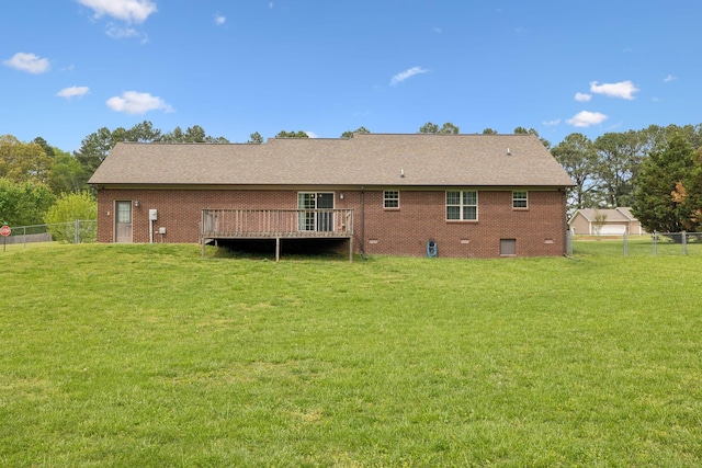 rear view of property featuring brick siding, fence, a wooden deck, and a lawn
