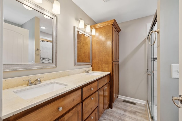 bathroom featuring double vanity, a sink, an enclosed shower, and wood finished floors