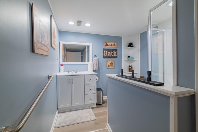 bathroom with wood finished floors, a shower with door, vanity, baseboards, and visible vents
