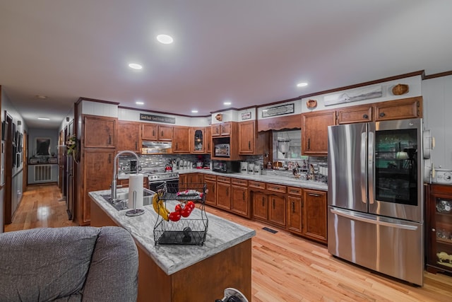 kitchen with stainless steel appliances, decorative backsplash, light wood finished floors, and a sink