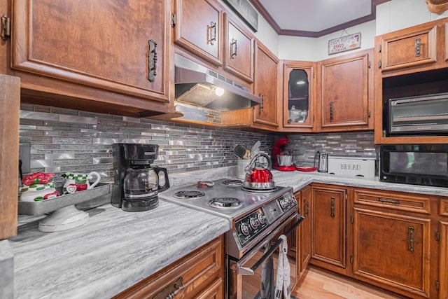 kitchen with brown cabinetry, range with electric cooktop, under cabinet range hood, light countertops, and crown molding