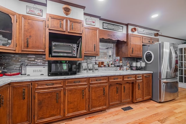 kitchen with black microwave, brown cabinets, crown molding, and freestanding refrigerator