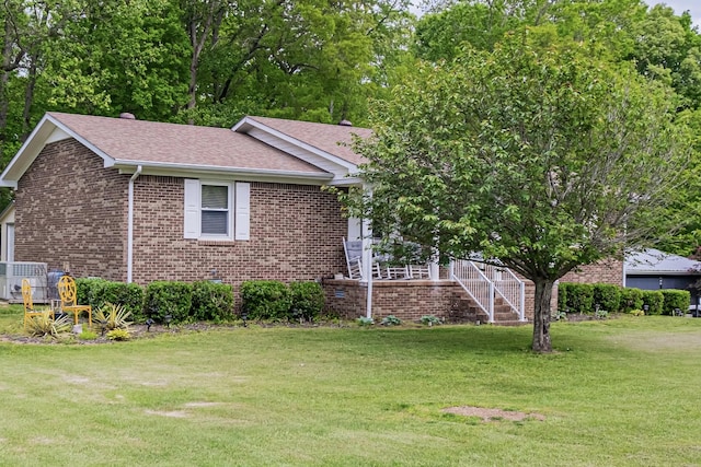 ranch-style home featuring roof with shingles, central AC unit, a front yard, and brick siding